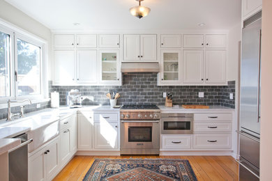 Example of a mid-sized transitional u-shaped medium tone wood floor open concept kitchen design in San Francisco with a farmhouse sink, glass-front cabinets, white cabinets, marble countertops, gray backsplash, cement tile backsplash, stainless steel appliances and no island