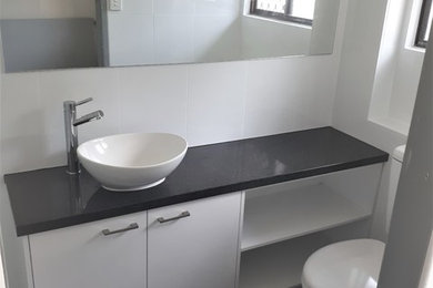 Photo of a mid-sized modern 3/4 bathroom in Gold Coast - Tweed with furniture-like cabinets, black cabinets, an open shower, a one-piece toilet, white tile, stone tile, white walls, ceramic floors, a console sink, laminate benchtops, grey floor and a sliding shower screen.