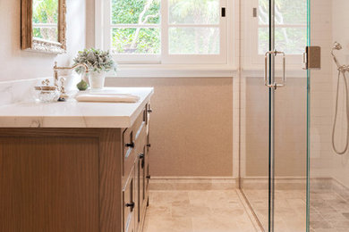 Photo of a small transitional bathroom in Los Angeles with shaker cabinets, medium wood cabinets, a corner shower, beige tile, subway tile, beige walls, marble floors, an undermount sink, marble benchtops, beige floor, a hinged shower door and white benchtops.