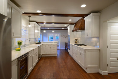 Design ideas for a large transitional l-shaped eat-in kitchen in Denver with a farmhouse sink, raised-panel cabinets, white cabinets, blue splashback, porcelain splashback, stainless steel appliances, dark hardwood floors, a peninsula and quartz benchtops.