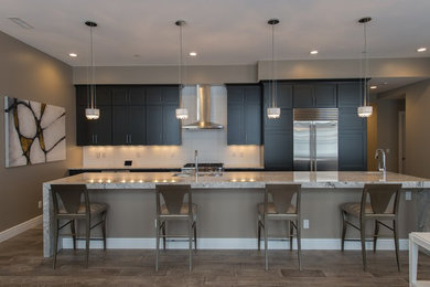Example of a mid-sized galley light wood floor and gray floor open concept kitchen design in Other with an undermount sink, flat-panel cabinets, black cabinets, quartz countertops, white backsplash, stone tile backsplash, stainless steel appliances and an island