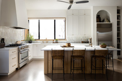 Photo of a mid-sized transitional l-shaped eat-in kitchen in Portland with an undermount sink, shaker cabinets, white cabinets, white splashback, stainless steel appliances, concrete floors, with island, brown floor and white benchtop.