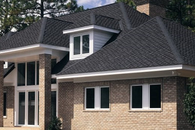 Example of a large classic beige two-story brick house exterior design in Charlotte with a hip roof and a shingle roof