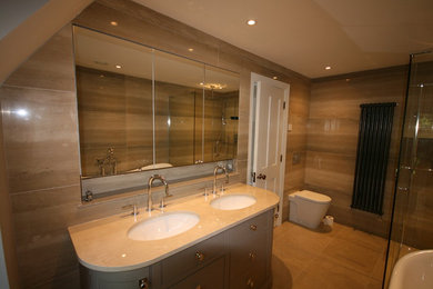 Medium sized modern ensuite bathroom in Other with an integrated sink, freestanding cabinets, grey cabinets, a freestanding bath, a built-in shower, a one-piece toilet, multi-coloured tiles, stone tiles, beige walls and limestone flooring.
