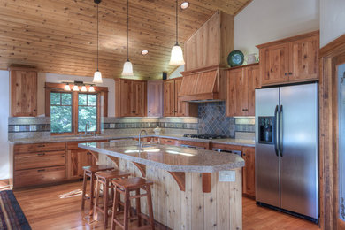 This is an example of a mid-sized arts and crafts l-shaped open plan kitchen in Sacramento with an undermount sink, shaker cabinets, medium wood cabinets, granite benchtops, grey splashback, stone slab splashback, stainless steel appliances, medium hardwood floors, with island and brown floor.