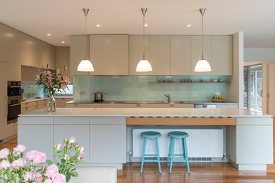 This is an example of a large contemporary open plan kitchen in Wollongong with with island, beige cabinets, stainless steel benchtops, blue splashback, glass sheet splashback, stainless steel appliances, a double-bowl sink and light hardwood floors.