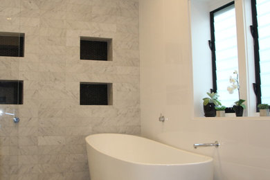 This is an example of a mid-sized contemporary master bathroom in Sydney with furniture-like cabinets, white cabinets, a freestanding tub, an open shower, a wall-mount toilet, black and white tile, porcelain tile, white walls, porcelain floors, an integrated sink and engineered quartz benchtops.