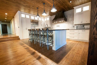 Large country u-shaped eat-in kitchen in Other with a farmhouse sink, shaker cabinets, white cabinets, granite benchtops, white splashback, subway tile splashback, stainless steel appliances, medium hardwood floors, with island and brown floor.