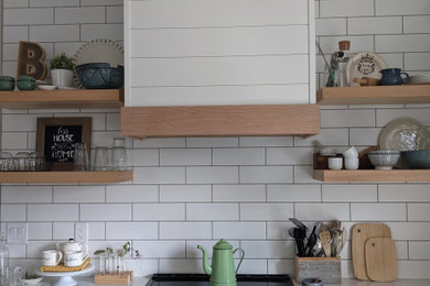 Inspiration for a mid-sized farmhouse l-shaped vinyl floor and brown floor eat-in kitchen remodel in Calgary with a farmhouse sink, shaker cabinets, white cabinets, quartzite countertops, white backsplash, subway tile backsplash, stainless steel appliances, an island and white countertops