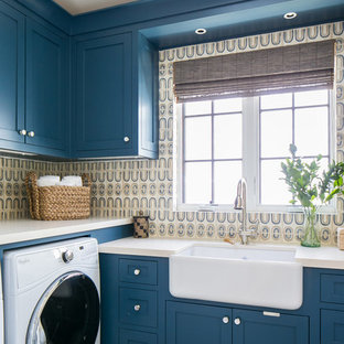 Diseño de cuarto de lavado en L, tropical, grande, con fregadero sobremueble, armarios estilo shaker, puertas de armario azules, paredes multicolor, lavadora y secadora juntas, suelo gris y encimeras beige