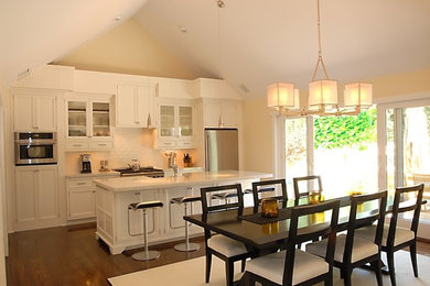 Inspiration for a mid-sized transitional l-shaped dark wood floor and brown floor eat-in kitchen remodel in Orange County with a farmhouse sink, recessed-panel cabinets, white cabinets, marble countertops, white backsplash, subway tile backsplash, stainless steel appliances and an island