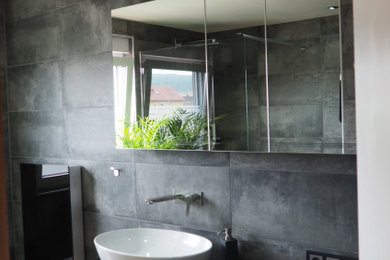 Kleines Modernes Duschbad mit bodengleicher Dusche, Wandtoilette, grauen Fliesen, Zementfliesen, grauer Wandfarbe, Fliesen in Holzoptik, Aufsatzwaschbecken, Mineralwerkstoff-Waschtisch, braunem Boden, offener Dusche, schwarzer Waschtischplatte, Wandnische und Einzelwaschbecken in Sonstige