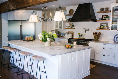 Large transitional u-shaped dark wood floor eat-in kitchen photo in Kansas City with a farmhouse sink, glass-front cabinets, white cabinets, marble countertops, white backsplash, subway tile backsplash, stainless steel appliances and an island