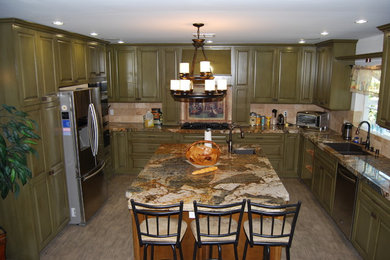 Inspiration for a large timeless u-shaped light wood floor enclosed kitchen remodel in Los Angeles with an undermount sink, raised-panel cabinets, green cabinets, granite countertops, beige backsplash, stone tile backsplash, stainless steel appliances and an island