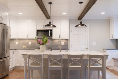 Inspiration for a large farmhouse l-shaped medium tone wood floor and brown floor eat-in kitchen remodel in Charlotte with a farmhouse sink, shaker cabinets, white cabinets, quartzite countertops, gray backsplash, glass tile backsplash, stainless steel appliances, an island and white countertops