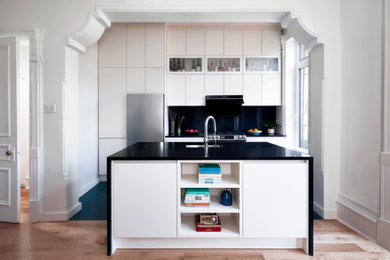 Eat-in kitchen - mid-sized modern single-wall porcelain tile and green floor eat-in kitchen idea with an undermount sink, flat-panel cabinets, white cabinets, granite countertops, black backsplash, granite backsplash, stainless steel appliances, an island and black countertops