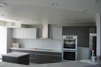 Eat-in kitchen - modern eat-in kitchen idea in Los Angeles with flat-panel cabinets, white backsplash, glass tile backsplash, stainless steel appliances and an island