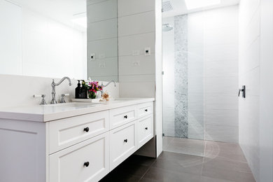Photo of a mid-sized transitional 3/4 bathroom in Melbourne with shaker cabinets, white cabinets, a curbless shower, a wall-mount toilet, white tile, porcelain tile, white walls, porcelain floors, an undermount sink, engineered quartz benchtops and grey floor.