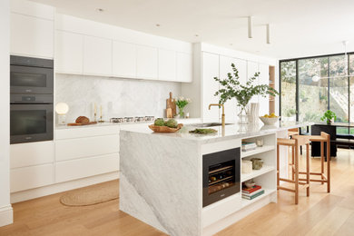 Inredning av ett modernt kök, med en dubbel diskho, vita skåp, svarta vitvaror, ljust trägolv, en köksö och brunt golv