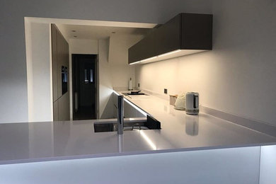 Large modern l-shaped kitchen in Hertfordshire with a built-in sink, quartz worktops, black appliances, a breakfast bar, white floors and white worktops.