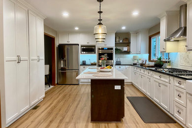 Inspiration for a large modern l-shaped laminate floor and multicolored floor eat-in kitchen remodel in Chicago with a farmhouse sink, recessed-panel cabinets, white cabinets, white backsplash, ceramic backsplash, stainless steel appliances, an island and black countertops