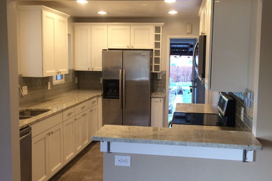 Inspiration for a timeless porcelain tile kitchen remodel in Denver with an undermount sink, shaker cabinets, white cabinets, granite countertops, gray backsplash, glass tile backsplash and stainless steel appliances