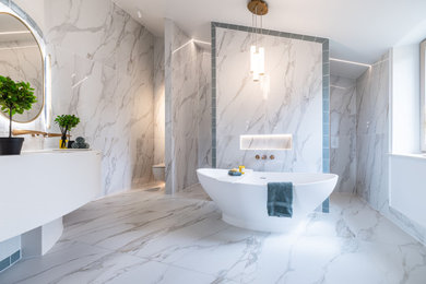 Photo of a large contemporary ensuite bathroom in Cambridgeshire with white cabinets, a freestanding bath, a double shower, a wall mounted toilet, multi-coloured tiles, white walls, solid surface worktops, an open shower, white worktops, feature lighting, double sinks and a built in vanity unit.