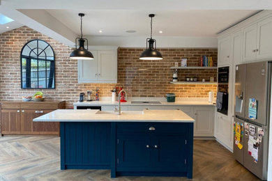 Inspiration for a large modern l-shaped open plan kitchen in Surrey with a belfast sink, blue cabinets, marble worktops, vinyl flooring, an island, brown floors and white worktops.
