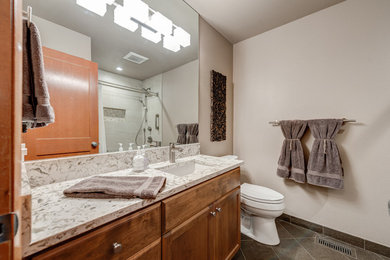 Mid-sized traditional kids bathroom in Portland with raised-panel cabinets, medium wood cabinets, a drop-in tub, a shower/bathtub combo, a two-piece toilet, multi-coloured tile, porcelain tile, beige walls, porcelain floors, an undermount sink, engineered quartz benchtops, brown floor and a shower curtain.