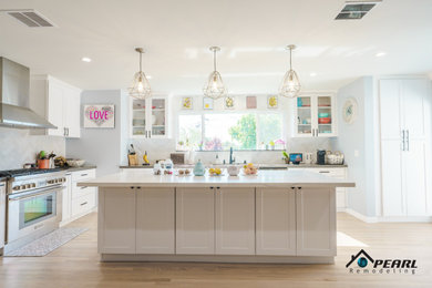 Large 1950s l-shaped light wood floor and beige floor eat-in kitchen photo in Los Angeles with a double-bowl sink, shaker cabinets, white cabinets, solid surface countertops, white backsplash, ceramic backsplash, stainless steel appliances, an island and gray countertops