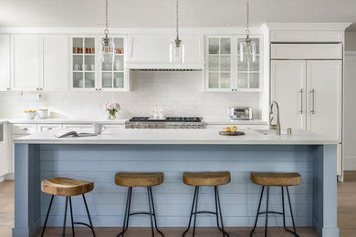 Inspiration for a mid-sized beach style kitchen in Sacramento with glass-front cabinets, white cabinets, white splashback, stainless steel appliances, medium hardwood floors, with island and brown floor.