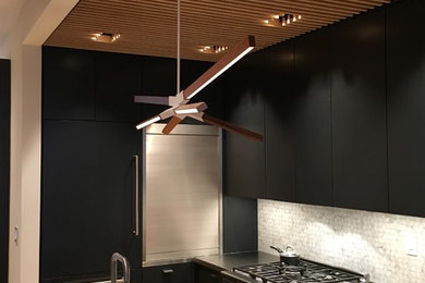 Small trendy l-shaped medium tone wood floor eat-in kitchen photo in New York with flat-panel cabinets, white backsplash, stainless steel appliances, an island, black cabinets, solid surface countertops, ceramic backsplash and an undermount sink