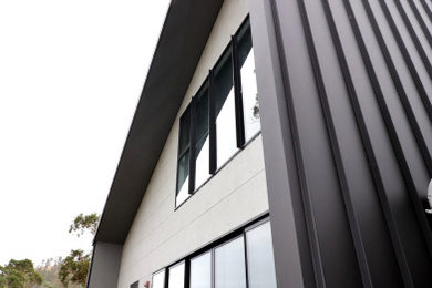 Contemporary two-storey grey house exterior in Hobart with metal siding, a metal roof and a black roof.
