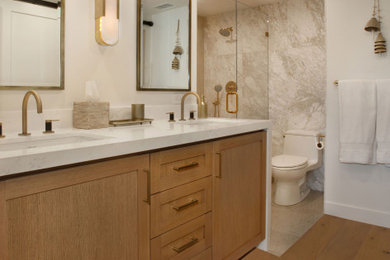 Inspiration for a small nautical ensuite bathroom in Orange County with shaker cabinets, medium wood cabinets, an alcove shower, a one-piece toilet, grey tiles, marble tiles, white walls, medium hardwood flooring, a submerged sink, engineered stone worktops, brown floors, a hinged door, white worktops, double sinks and a built in vanity unit.