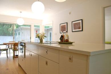 Mid-sized minimalist galley light wood floor eat-in kitchen photo in Raleigh with a farmhouse sink, flat-panel cabinets, gray cabinets, quartz countertops, gray backsplash, cement tile backsplash, stainless steel appliances and an island