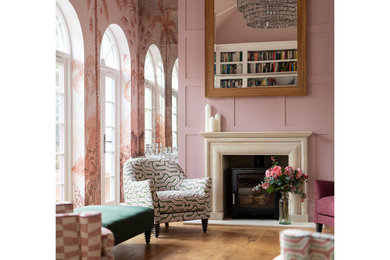 Aménagement d'un grand salon classique ouvert avec une salle de musique, un mur rose, parquet clair, un poêle à bois, un manteau de cheminée en pierre, un sol beige et un plafond voûté.