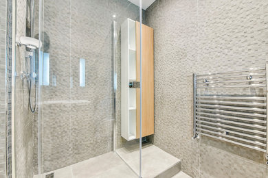 Photo of a small contemporary kids wet room bathroom in London with flat-panel cabinets, light wood cabinets, a wall-mount toilet, gray tile, ceramic tile, grey walls, porcelain floors, a wall-mount sink, grey floor and a hinged shower door.