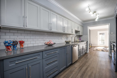 Example of a mid-sized minimalist galley laminate floor and brown floor enclosed kitchen design in Houston with an undermount sink, raised-panel cabinets, white cabinets, quartz countertops, white backsplash, ceramic backsplash, stainless steel appliances, gray countertops and no island