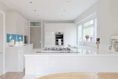 Large modern l-shaped open plan kitchen in Essex with a belfast sink, flat-panel cabinets, white cabinets, quartz worktops, blue splashback, glass sheet splashback, stainless steel appliances, vinyl flooring and a breakfast bar.