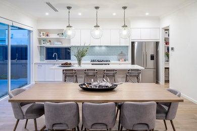 Inspiration for a mid-sized beach style galley open plan kitchen in Perth with a drop-in sink, shaker cabinets, white cabinets, marble benchtops, blue splashback, subway tile splashback, stainless steel appliances, light hardwood floors, with island, brown floor and white benchtop.