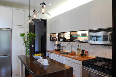 Example of a mid-sized eclectic galley light wood floor kitchen design in New York with a drop-in sink, flat-panel cabinets, white cabinets, wood countertops, white backsplash, stone tile backsplash, stainless steel appliances and an island
