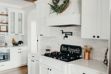 Example of a large country l-shaped medium tone wood floor and brown floor eat-in kitchen design in Charlotte with an undermount sink, recessed-panel cabinets, white cabinets, quartz countertops, white backsplash, stone tile backsplash, stainless steel appliances, an island and white countertops