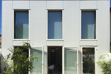 Cette image montre une petite façade de maison de ville métallique et blanche design à un étage avec un toit plat et un toit mixte.
