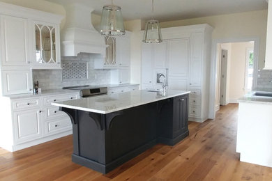 Immagine di un cucina con isola centrale chic con ante bianche, paraspruzzi bianco, elettrodomestici in acciaio inossidabile e parquet chiaro