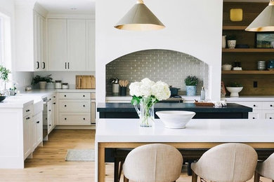 Example of a mid-sized 1960s light wood floor kitchen design in Salt Lake City with a farmhouse sink, white cabinets, subway tile backsplash, stainless steel appliances, two islands and white countertops