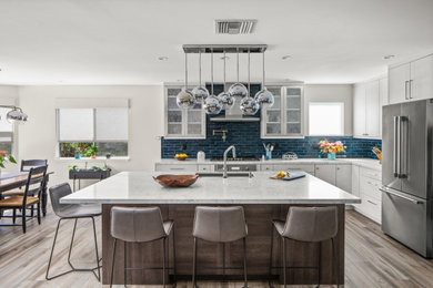 Mid-sized transitional l-shaped porcelain tile and gray floor open concept kitchen photo in San Diego with an undermount sink, recessed-panel cabinets, white cabinets, quartz countertops, blue backsplash, ceramic backsplash, stainless steel appliances, an island and multicolored countertops