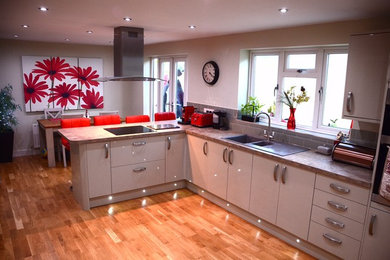 Photo of a mid-sized contemporary l-shaped eat-in kitchen in West Midlands with grey cabinets, laminate benchtops, black appliances, laminate floors and a peninsula.