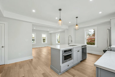 Photo of a large modern single-wall eat-in kitchen in Boston with an undermount sink, shaker cabinets, grey cabinets, quartz benchtops, white splashback, engineered quartz splashback, stainless steel appliances, light hardwood floors, with island, beige floor, white benchtop and recessed.
