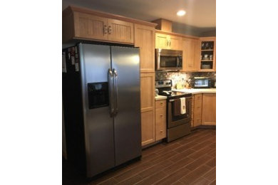 Inspiration for a timeless l-shaped porcelain tile and brown floor eat-in kitchen remodel in Austin with an undermount sink, light wood cabinets, quartz countertops, glass tile backsplash, stainless steel appliances and a peninsula