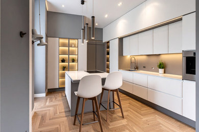 Esempio di una cucina minimalista di medie dimensioni con lavello a doppia vasca, ante lisce, ante grigie, paraspruzzi bianco, elettrodomestici neri, top in superficie solida, parquet chiaro, pavimento marrone e top bianco